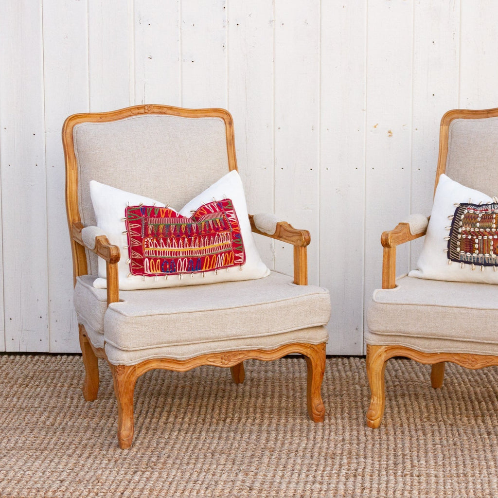 Two wooden chairs with beige cushions and decorative pillows against a white paneled wall.