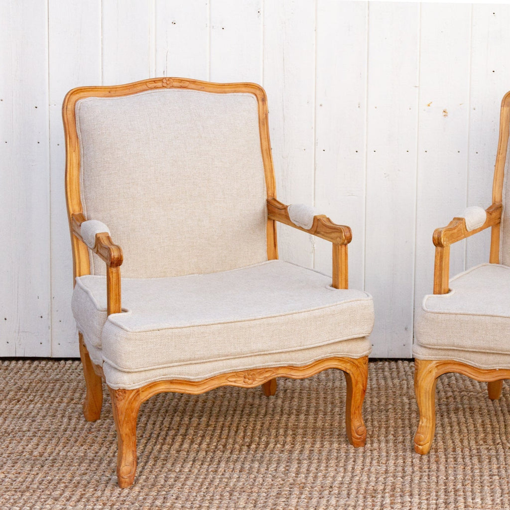 Pair of wooden armchairs with beige cushions on a textured floor.