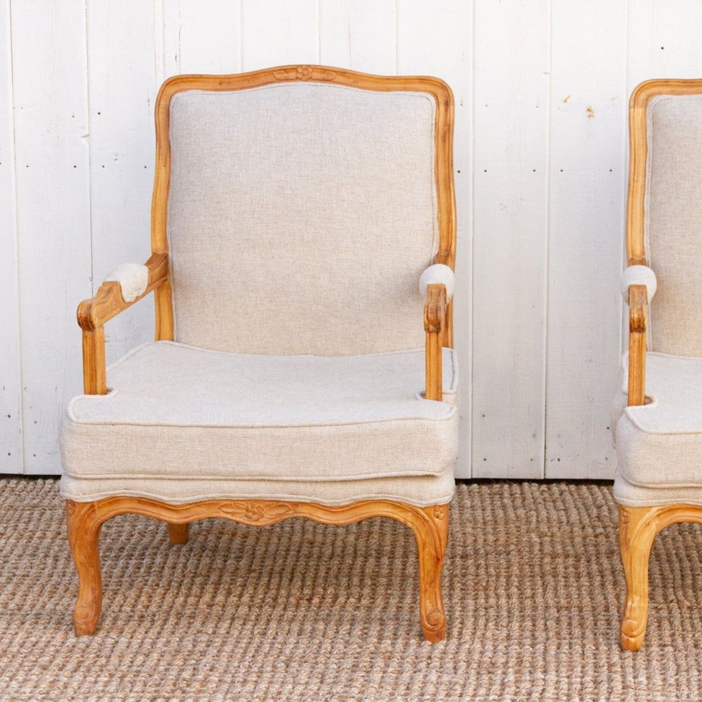 Two wooden armchairs with beige cushions on a textured floor.