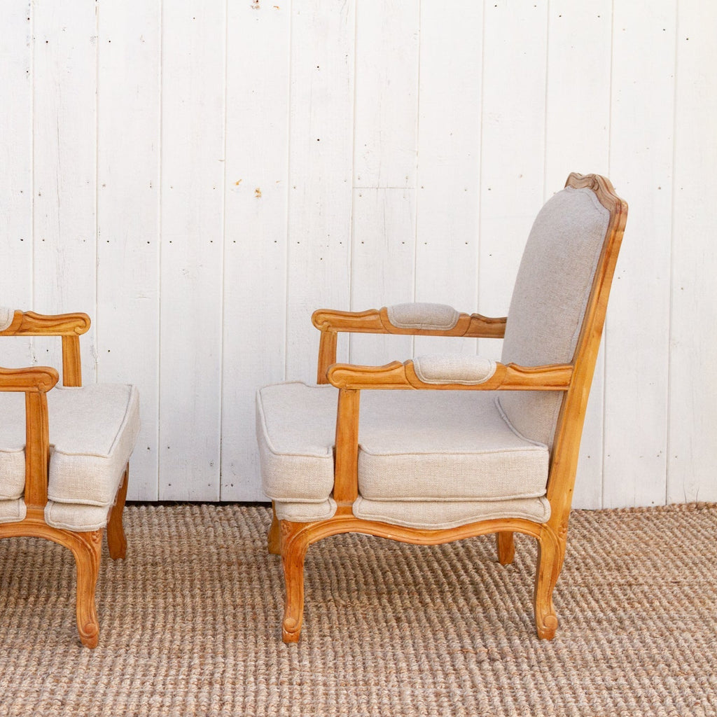 Pair of wooden armchairs with beige cushions against a white paneled wall.