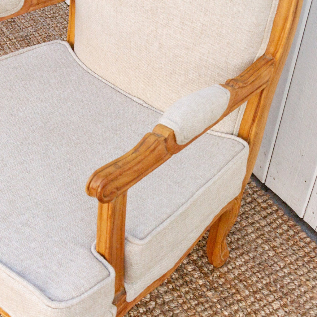 Chair with wooden armrests and white cushion on a textured floor.