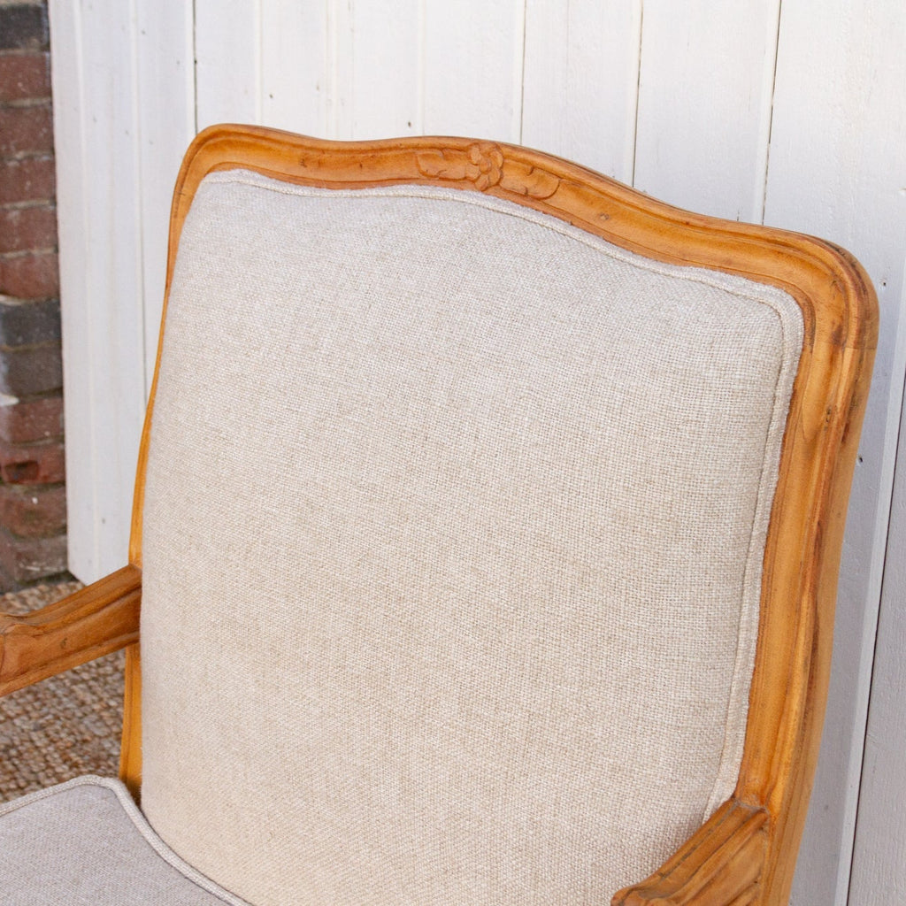 Chair with wooden frame and beige cushion against a white wall.