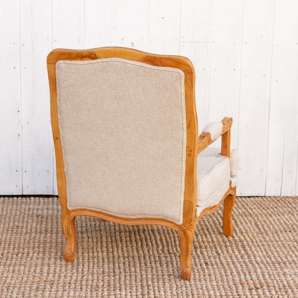 Wooden armchair with beige cushion against a white paneled wall.