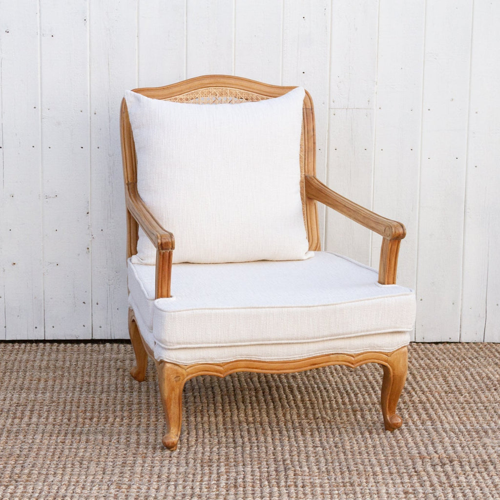 Wooden armchair with white cushion against a white wooden paneled wall.