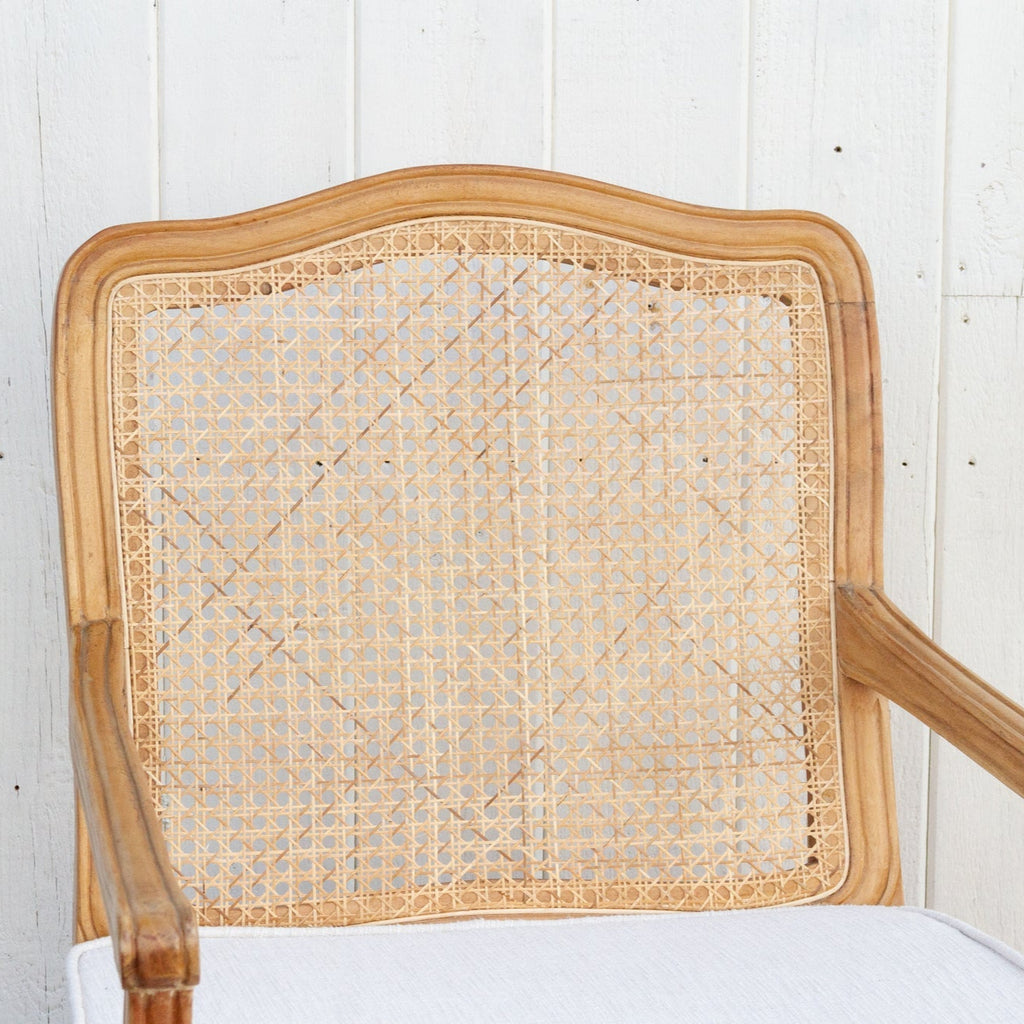 Antique caned chair with white cushion against a white wooden panel background