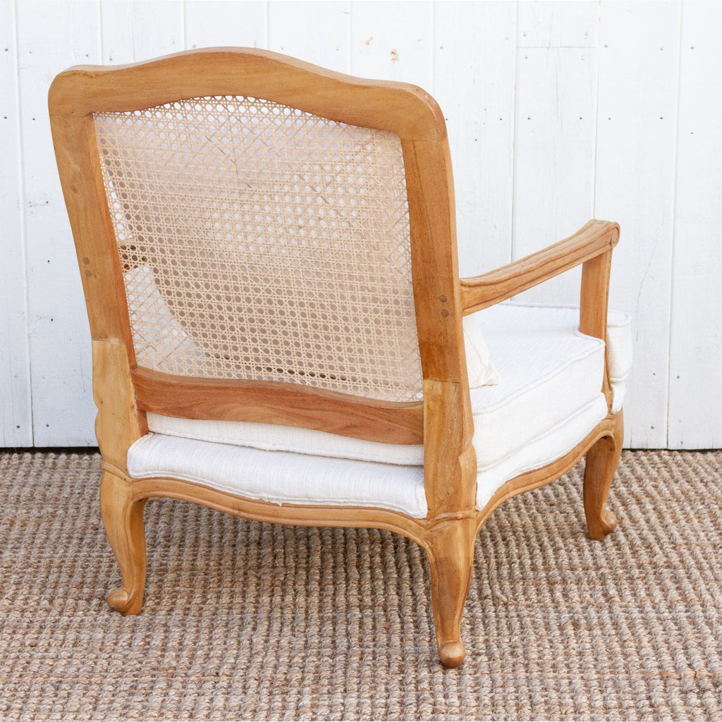Wooden armchair with caned backrest and white cushion on a textured floor.